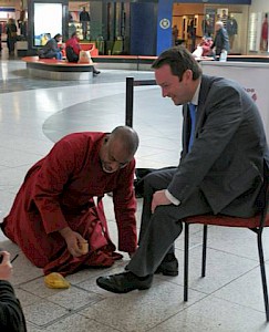 The Dean shines the shoes of David Allinson, Centre Director of Manchester Arndale